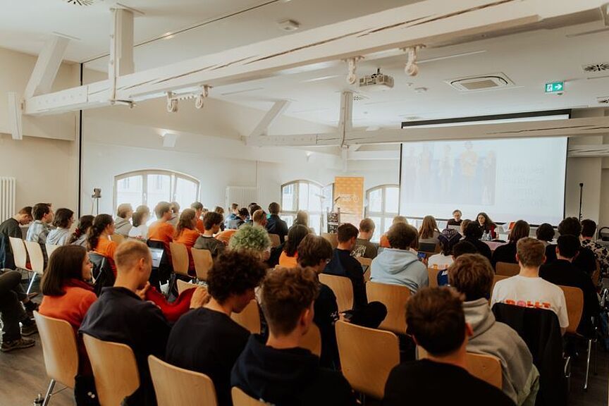 ADFC-Bundesjugendversammlung Junge Menschen sitzen auf Stühlen in einem große Saal und schauen nach vorn auf eine Leinwand.